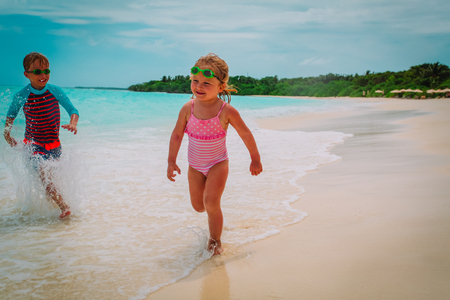 little girl and boy run play with waves on beachの写真素材