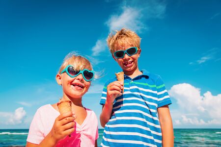 happy kids- boy and girl- eating ice cream on beachの写真素材