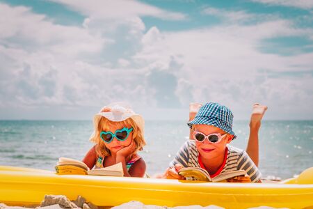 cute boy and girl reading books at beach vacationの写真素材