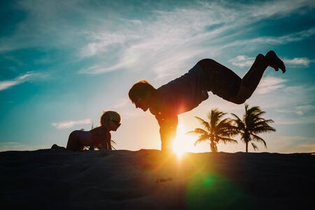 father and little daughter silhouettes exercise and have fun at sunsetの写真素材