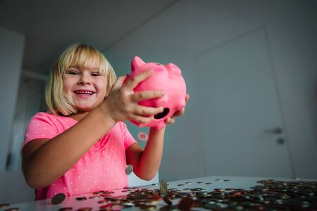 happy little girl taking coins from piggy bankの写真素材
