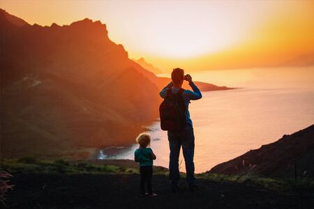 father with little daughter hiking in mountains, dad making photos of scenic sunsetの写真素材