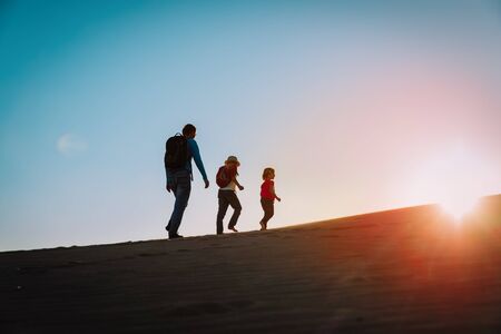 Silhouettes of father with son and daughter hiking at sunset