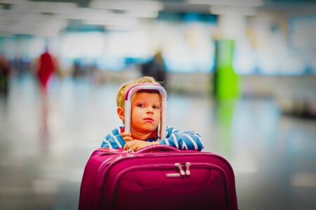cute little boy with suitcase waiting in the airportの写真素材