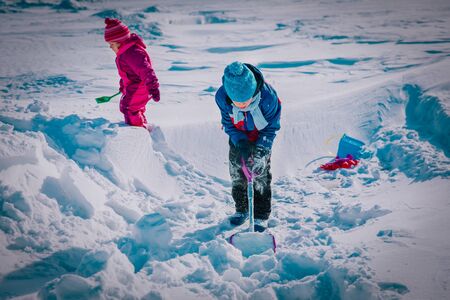 kids -boy and girl- digging snow in winter, kids seasonal fun