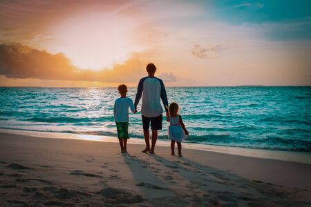 father and kids walking on beach at sunsetの写真素材