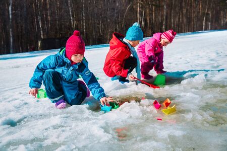 kids play with paper boats in spring puddle