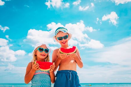 happy boy and girl eating watermelon at beachの写真素材