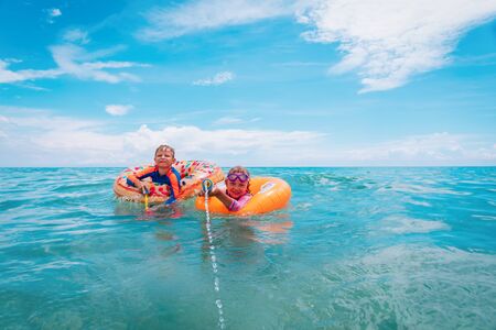 happy boy and girl play with water guns while floating on beachの写真素材