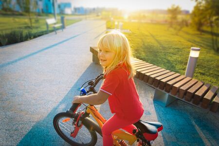 cute happy little girl riding bike at sunsetの写真素材
