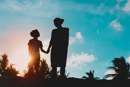 silhouettes of mother and son holding hands at sunset beachの写真素材