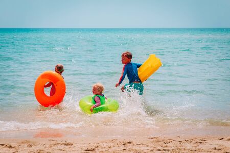 happy boy and girls with floaties run swim on beach, family at sea