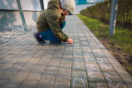 little girl writing numbers on asphalt, kid playing outside while school is closedの写真素材