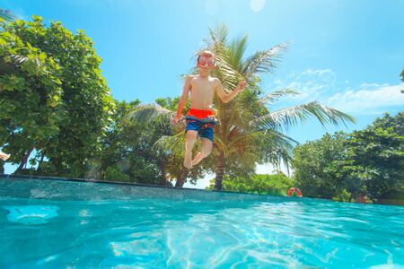 Happy boy jumping into swimming pool, kid on vacationの写真素材