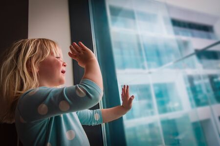Little girl staying home, child waving hand to her family or friends outside