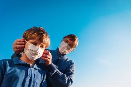 Father puts a medical mask on her son on skyの写真素材