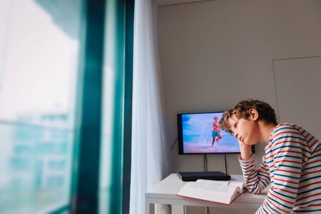 sad boy reading and doing homework at home while dreaming of beach vacation, stress and anxietyの写真素材