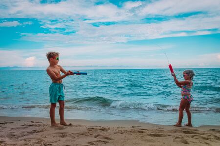 happy cute boy and girl play with water guns on beachの写真素材
