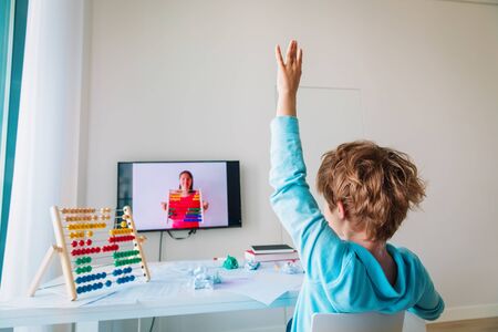 kid learning at home, boy raising hand doing online math lesson