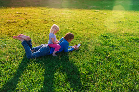 father and little daughter reading and looking at mobile phone on summer green grass