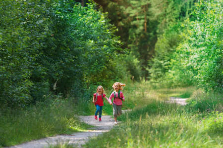happy little girls with backpacks run in natureの写真素材