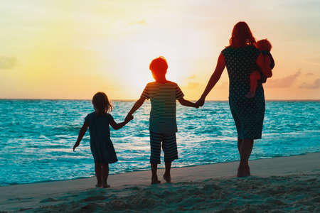 mother with kids walking on beach at sunsetの写真素材