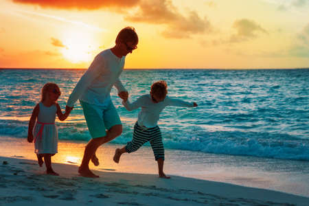 father with son and daughter play on beach at sunset