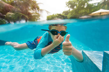 happy little boy swimming underwater with thumbs up on tropical resort