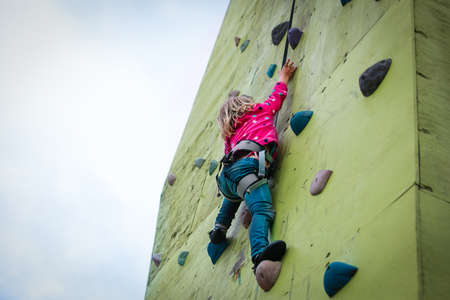 little girl climbing on artificial boulders wall outsideの写真素材