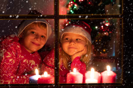 boy and girl looking at Christmas candles viewed from outside windowの写真素材