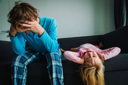 father is tired and stressed while daughter plays and makes noiseの写真素材