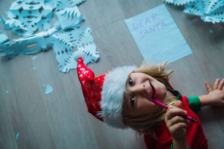 happy little girl writing letter to Santa and making snowflakes from paper