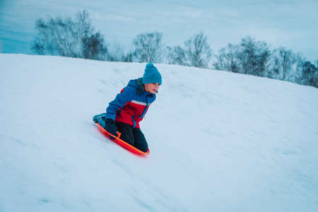 happy kid sliding on sled down snow hill outdoors in winterの写真素材