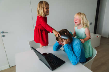 father is working from home while little daughters are combing himの写真素材