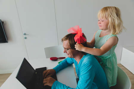father is working from home while little daughter making his hairstyleの写真素材