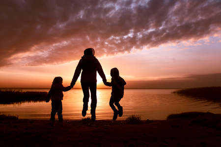 happy mother with kids looking at sunset on lake