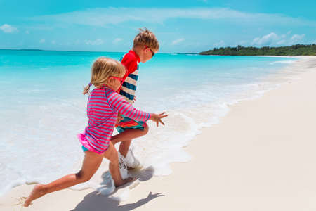 happy girl and boy run play with waves on beachの写真素材