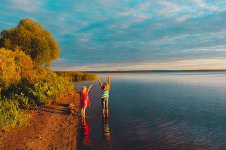 happy little girls enjoy sunset on lakeの写真素材