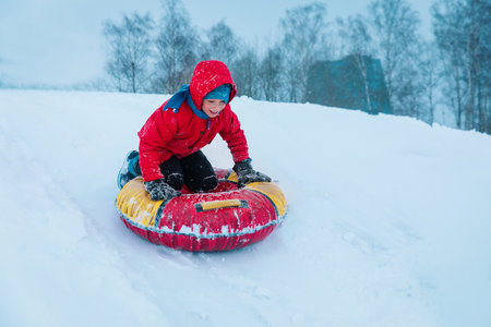 happy kid sliding on tube down snow hill outdoors in winterの写真素材