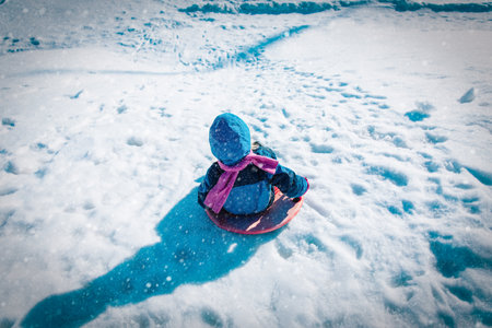 kids winter fun- little girl sliding in winter snowの写真素材