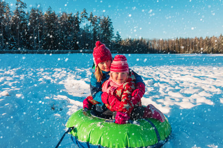 happy little girls slide in winter snow, kids have fun outsideの写真素材