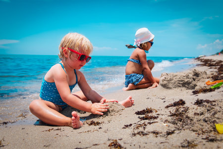 cute little girls play with sand on beachの写真素材