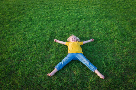 cute happy girl relaxing lying down on green grass in summerの写真素材