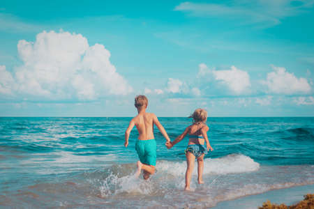 little girl and boy run and play with water at beachの写真素材
