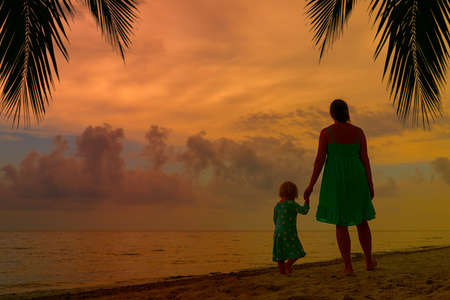 mother and little daughter walking on beach at sunsetの写真素材