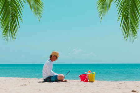 man with laptop on tropical beach vacation, family holiday at seaの写真素材