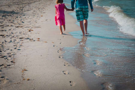 father and daughter walking on beach leaving footprint in sandの写真素材
