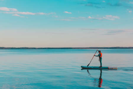 Kid riding on paddle sup surfboard in water at sunsetの写真素材