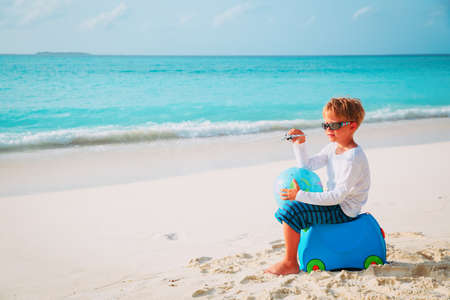 travel to beach-little boy with toy plane, globe and luggage at seaの写真素材