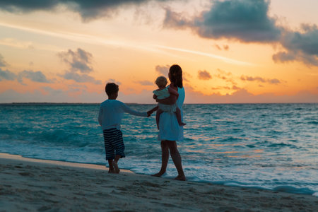 mother and two kids walking at sunset beachの写真素材